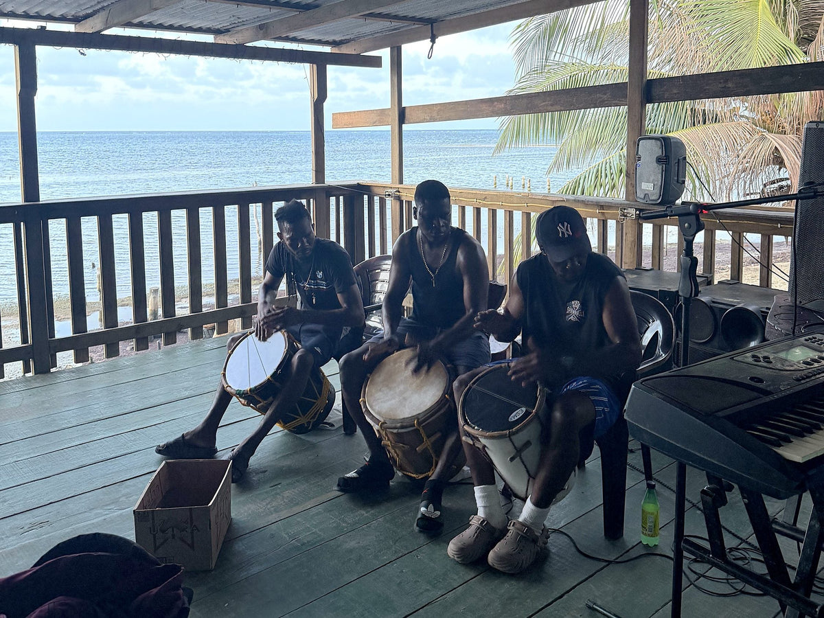 Three Garifuna drummers playing on a seafront deck in Punta Gorda, Roatan